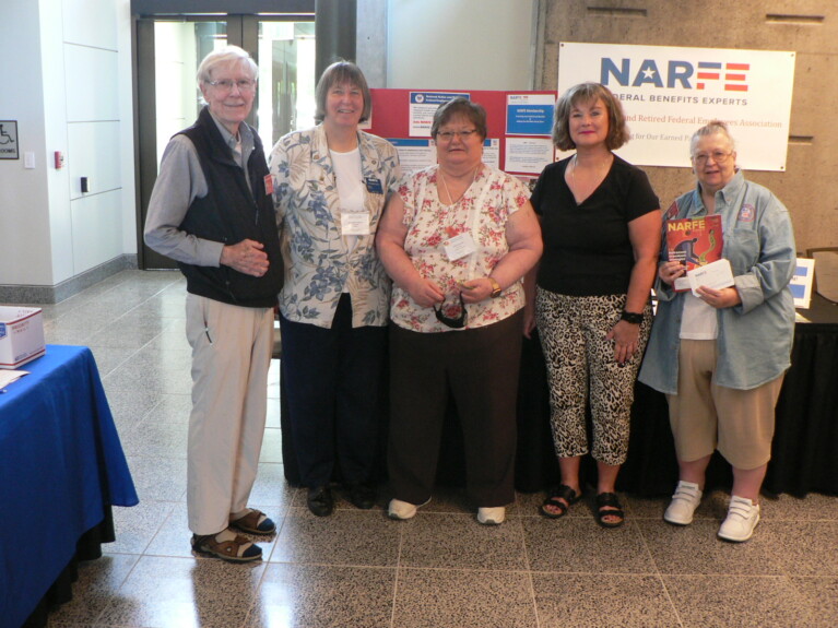 Five people standing in front of a table at an event displaying information about NARFE.