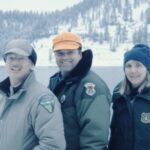 Three people wearing winter jackets with agency patches.