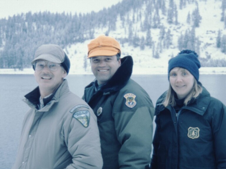 Two men and one woman wearing winter jackets displaying agency patches.