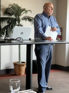 Man dressed in blue standing behind table.