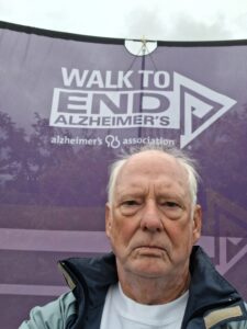 Man stands in front of purple sign reading Walk to End Alzheimer's.