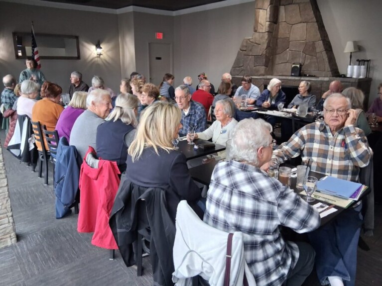Numerous people sitting around dining tables.