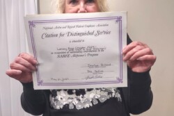 Person standing holding an award certificate in front of her.