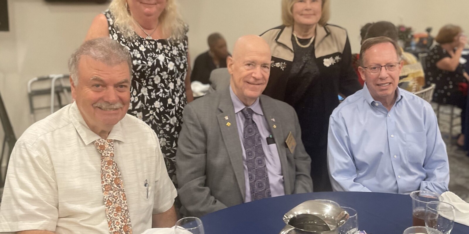 Picture of five people, three seated and two standing behind them by a table they held a dinner at before taking the picture