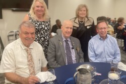 Picture of five people, three seated and two standing behind them by a table they held a dinner at before taking the picture