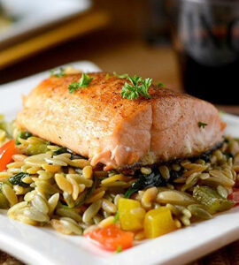 A picture of a cooked slice of salmon over a bed of rice and mixed veggies.
