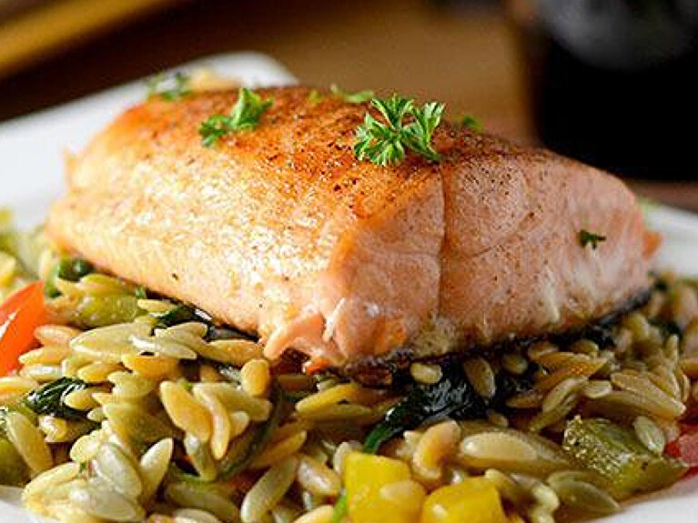 A picture of a cooked slice of salmon over a bed of rice and mixed veggies.