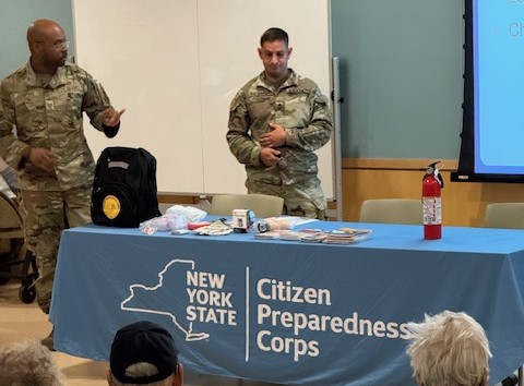 Two men in military uniforms standing behind table with cloth for New York State Citizen Preparedness Corps.