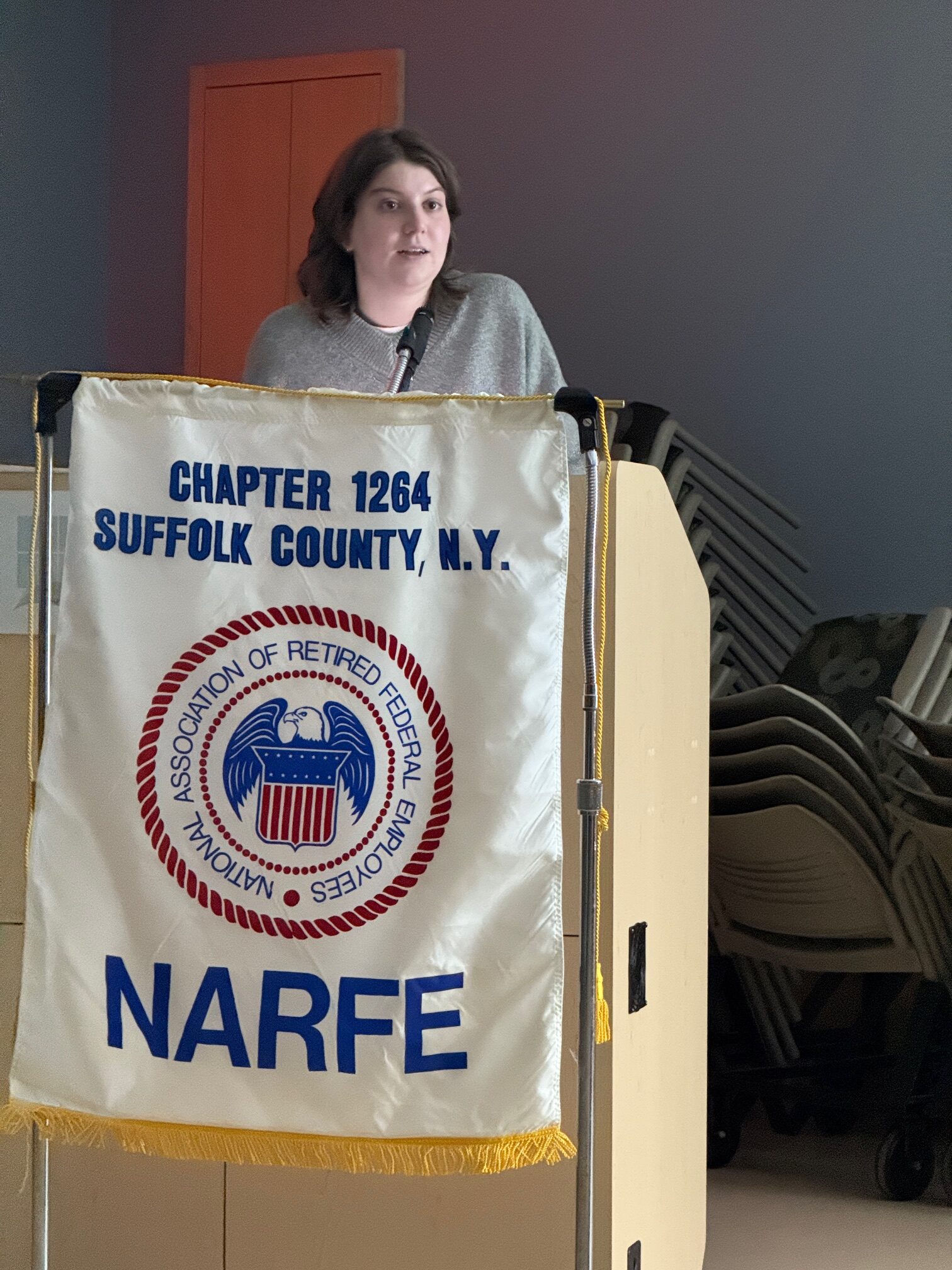 Women standing behind podium with NARFE Chapter 1264 Flag.