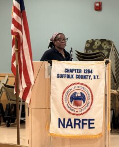 Women standing behind podium next to American Flag.