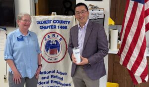 Chapter 1466 President and guest speaker holding NARFE tumbler standing in front of chapter banner