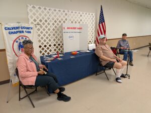 3 adults sitting around table with banners, posters and US flag