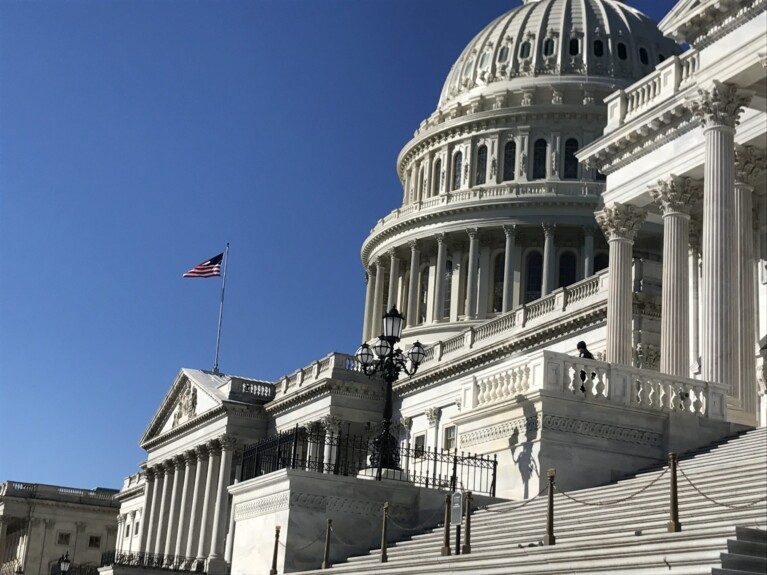 US Capitol dome in a clear blue sky with the American flag flying in the breeze