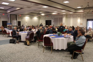woman standing in a hotel conference room with others seated at tables
