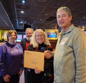 Woman presenting an envelop to a man with others looking on in a restaurant dining room