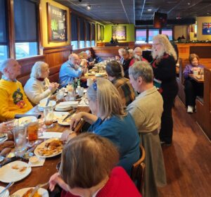 woman speaking to a group gathered at a meal in a restaurant dining room