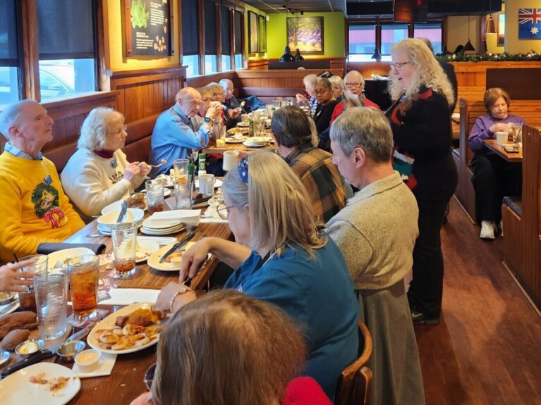 woman speaking to a group gathered at a meal in a restaurant dining room