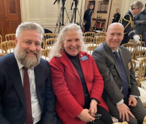 White House East Room setting up for bill signing with three seated, rows of empty chairs, television cameras, and uniformed service members.