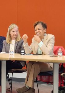 Two women sitting at a table of panelists in front of an orange wall