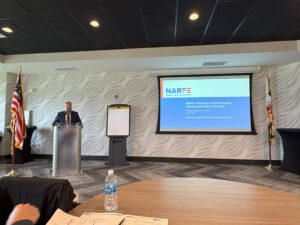 Man at podium between flag and NARFE PowerPoint slide projected on screen