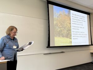 woman at podium by slide of trees with fall leaves and poem