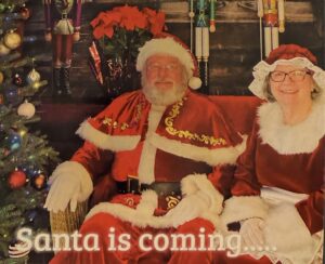 Santa and Mrs. Claus by a Christmas tree in front of nutcrackers and a pointsettia