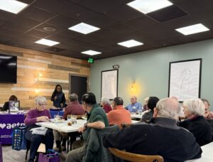 Woman standing at the front of a dining room speaking to a group.