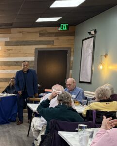Man standing in front of tables of people.