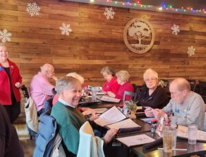8 people at holiday lunch in front of wood paneled restaurant with decorative snowflakes and colorful lights