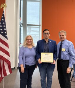 three people and a certificate in front of a flag