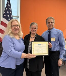 three people and a certificate in front of a flag
