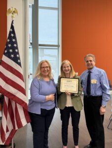 three people and a certificate in front of a flag