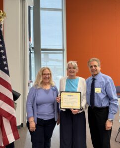 three people and a certificate in front of a flag