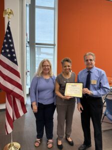 three people and a certificate in front of a flag