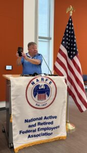man at podium with NARFE logo banner beside American flag