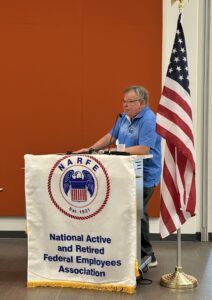 man at podium with NARFE logo banner beside American flag