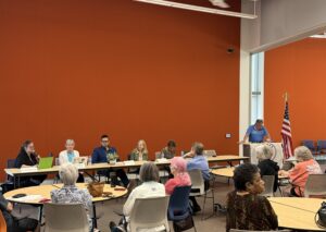 long table with panelists and a podium in front of an audience at round tables