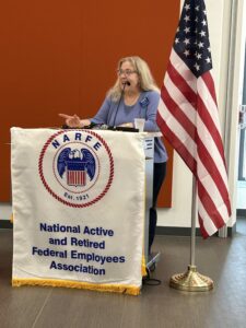 woman at podium with NARFE logo banner beside American flag