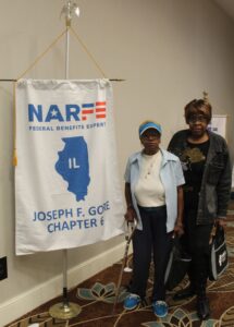 two ladies standing t right of their chapter banner hanging from a stand
