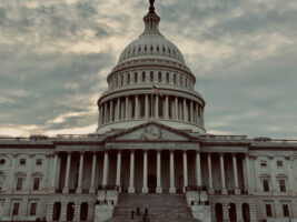 concrete building with tri-level done in center, US flag flying over main entrance with 15 columns below it and long, wide staircase down the middle