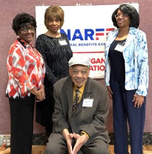 Three Chapter members standing and one sitting in front of banner on a wall
