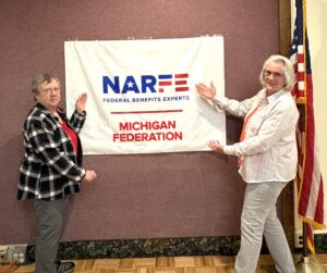 One Chapter member her guest standing in front of banner on a wall