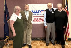 Four Chapter members standing in front of banner on a wall