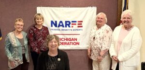 Five women members standing in front of banner on a wall