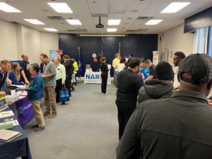 Display tables of NARFE and Health insurance info with a large group of people chatting and interacting