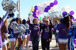 People at a Walk for Alzheimer's event, wearing Alzheimer's shirts with purple and white balloons in the background.