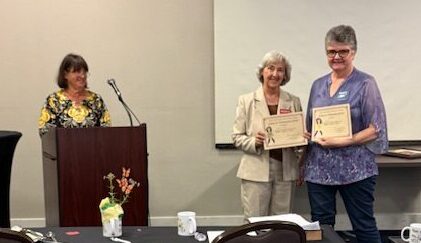 Woman at podium and two women holding certificates