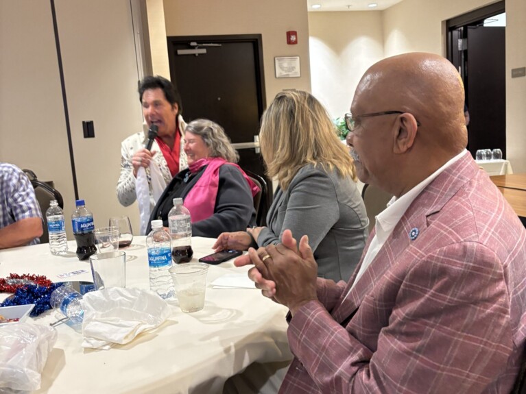 Elvis is singing into a wireless microphone and crooning to a member in a black jacket and pink scarf.