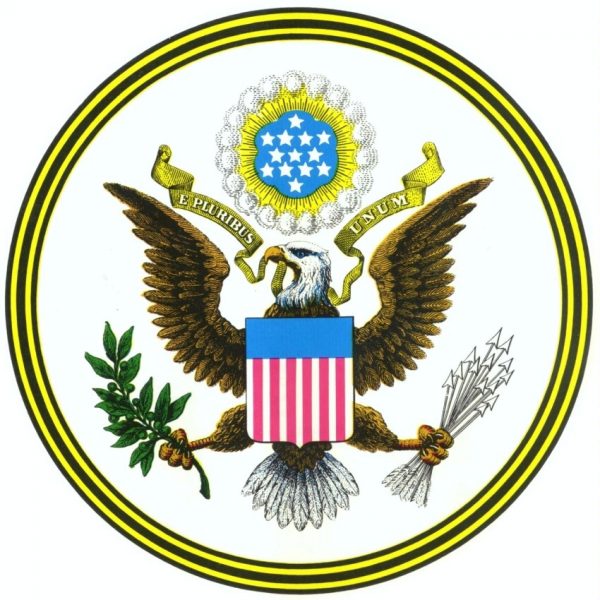 colored image of Great Seal of the United States with eagle holding banner in his beak reading E PLURIBUS UNUM, red, white & blue shield on his chest, an olive branch in his right claw and arrows in his left claw. A cloud above his head holds thirteen white stars on a blue background with a small gold circle and a larger white circle around it. The circular border has five alternating bands of black and gold colors.