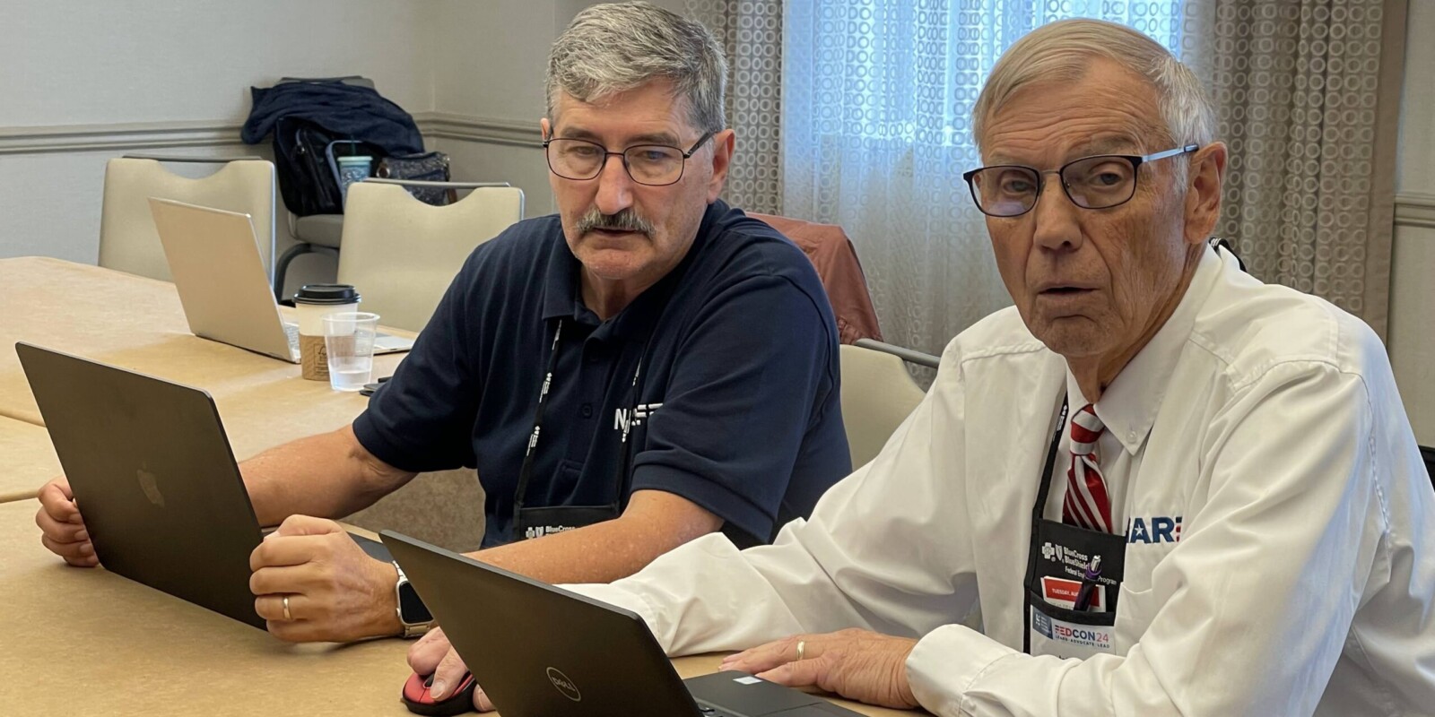 two men with laptops looking up at camera